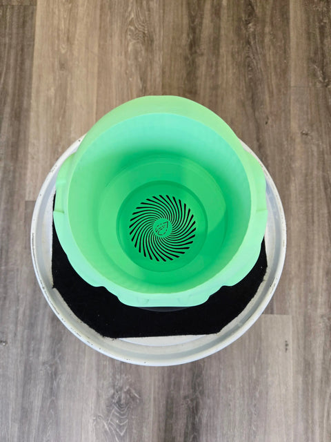 Green plastic bucket with a spiral pattern on the bottom, sitting inside a white container.