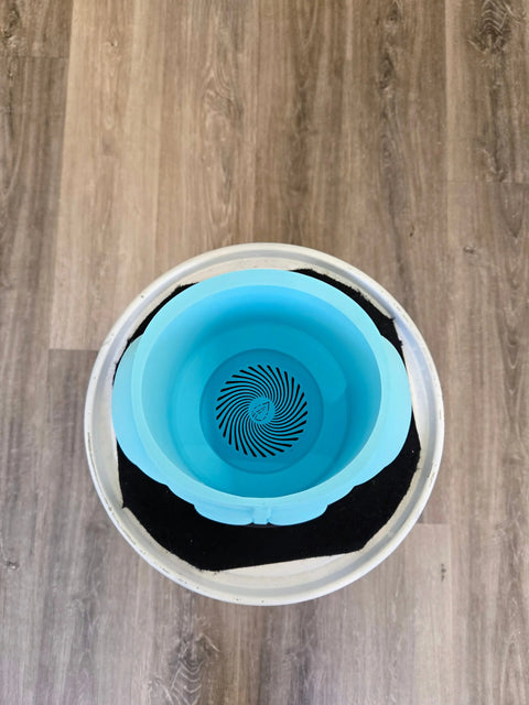 Circular blue pet water bowl with a spiral pattern at the bottom, sitting inside a white container with a black mat.