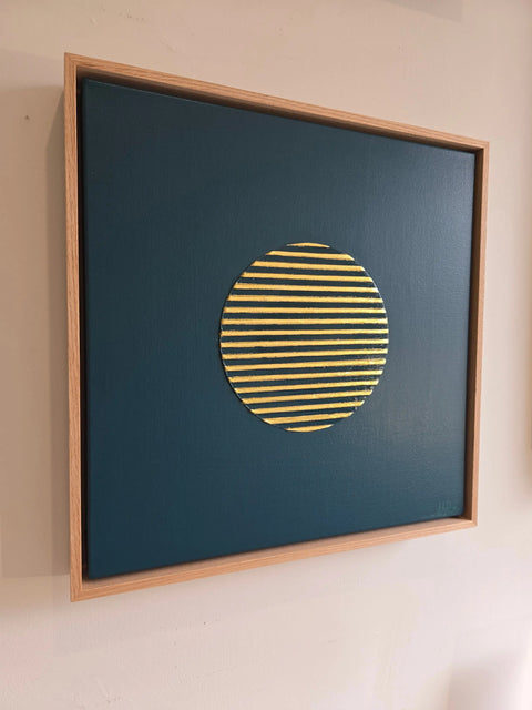 Framed artwork featuring a yellow striped circle on a dark blue background.