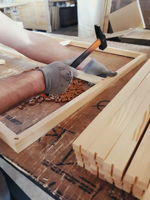 Wooden frame being assembled with a hammer and gloved hand.