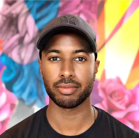 Man in a black baseball cap and t-shirt against a vibrant background in Yannick Aaron collection.