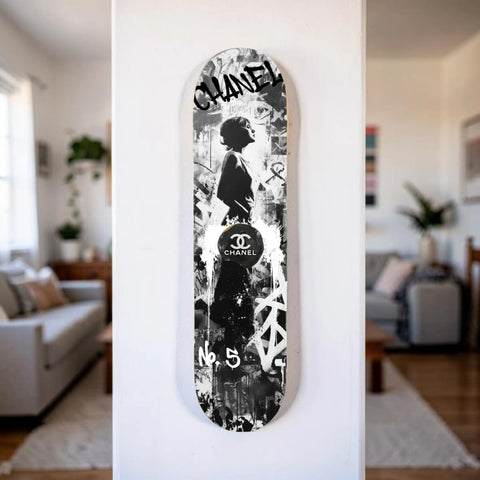 A black and white chanel skateboard deck featuring a stylized silhouette, graffiti-style graphics, and the iconic cc logo.