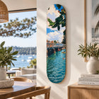 A vertically oriented skateboard deck painted with people swimming under a bright sky brunswick heads Australia keepsake fakeboard