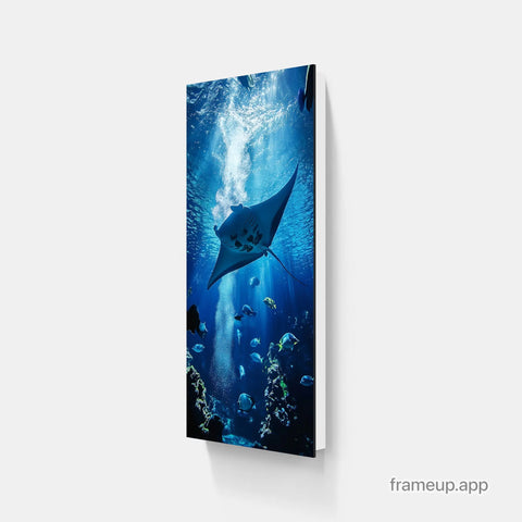 A vertical canvas print featuring a majestic manta ray gliding through deep blue ocean waters, surrounded by schools of fish and illuminated by sunbeams piercing the surface.
