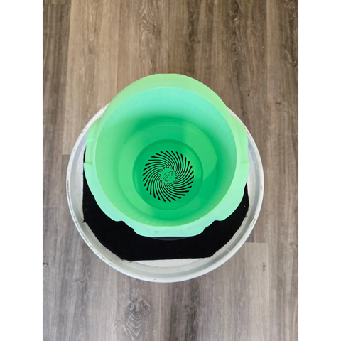 Green plastic bucket with a spiral pattern on the bottom, sitting inside a white container.