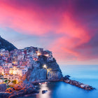 Pink and purple sky over cliffside town with colorful buildings.