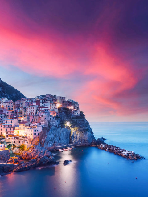 Pink and purple sky over cliffside town with colorful buildings.