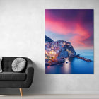 Modern black leather sofa with silver pillow and white cushion.assistant: vibrant cityscape canvas print featuring illuminated buildings against a sunset sky, mounted on wall above dark gray couch adorned with metallic accent pillows.