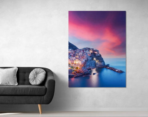 Modern black leather sofa with silver pillow and white cushion.assistant: vibrant cityscape canvas print featuring illuminated buildings against a sunset sky, mounted on wall above dark gray couch adorned with metallic accent pillows.