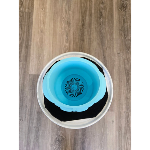 Circular blue pet water bowl with a spiral pattern at the bottom, sitting inside a white container with a black mat.
