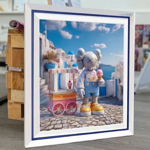 White-framed artwork featuring a kaws character in light gray with yellow shoes, holding an ice cream cone beside a pink and white cart labeled ’kool kreamery’ against a backdrop of blue-domed buildings.
