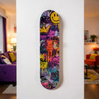 Vibrant purple skateboard deck adorned with colorful graffiti art and a central orange bear figurine.