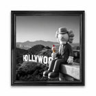 A black-framed canvas print featuring a kaws character in a pinstripe suit holding ice cream against a grayscale hollywood sign