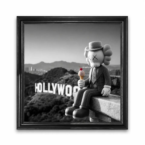 A black-framed canvas print featuring a kaws character in a pinstripe suit holding ice cream against a grayscale hollywood sign
