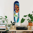 Colorful, abstract portrait painted on a skateboard deck mounted vertically on a wall.